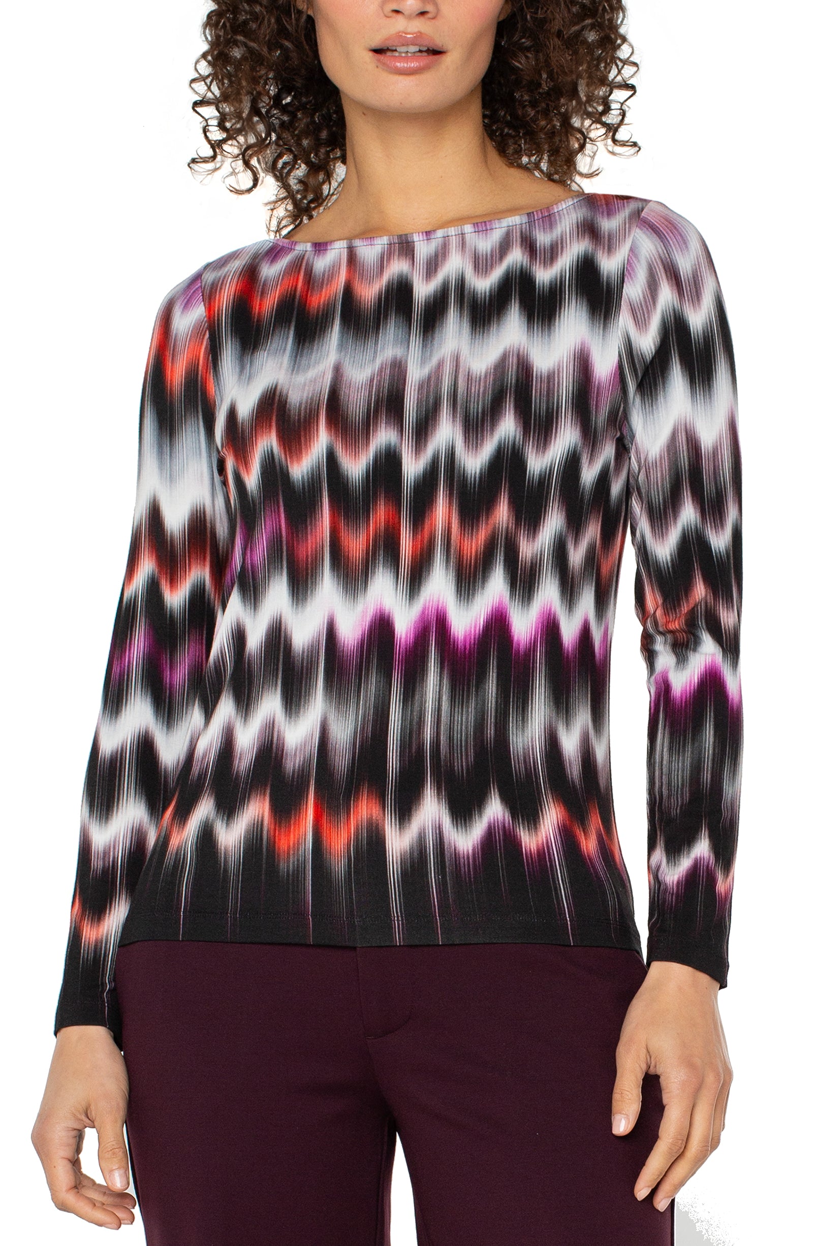 Woman wearing a colorful zigzag patterned top with maroon pants.