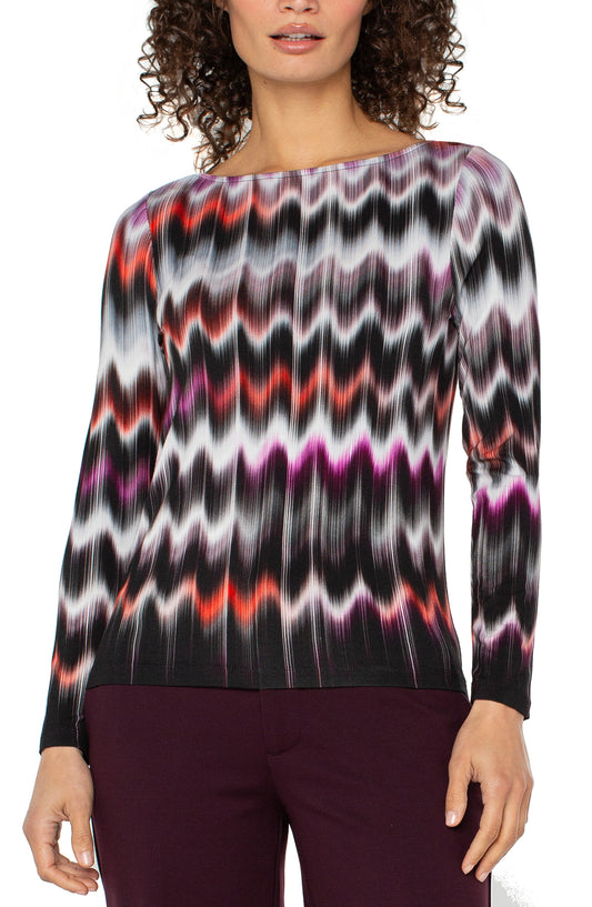Woman wearing a colorful zigzag patterned top with maroon pants.